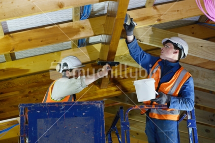 Tradesman painting the beams inside a wooden industrial building