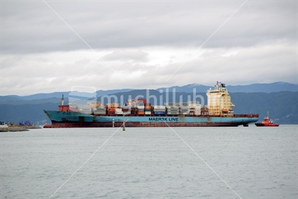 Tug boats guide a container ship into port at Wellington