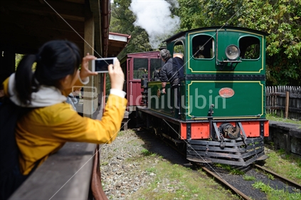 An Asian tourist photographs the Shantytown steam train on her smartphone.