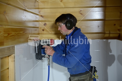 A builder staples off waterproof wall cladding in a bathroom