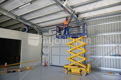 A plumber installs insulated water pipes from the safety of a scissor lift into the roof of a new commercial building