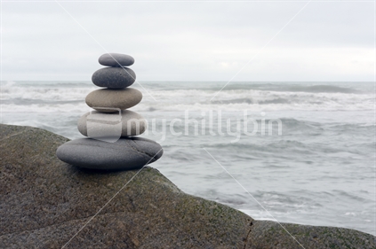 Five smooth stones balance on a rock at a West Coast beach, South Island, New Zealand