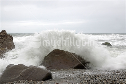 A slow shutter seed captures a wave crashing onto rocks during low tide at a West Coast beach, South Island, New Zelaand