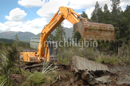 Excavator digging drainage channels in swampy land on the West Coast