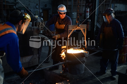 A foundryman removes slag from the top of a ladel of molten iron. 
