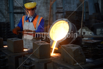 Foundrymen pour molten iron into moulds for making fire grates. (Shot in available light with shallow depth of field.)