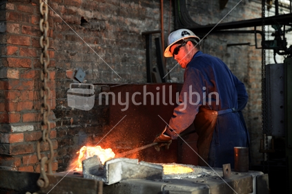 A foundryman clears slag from the molten iron in the furnace.