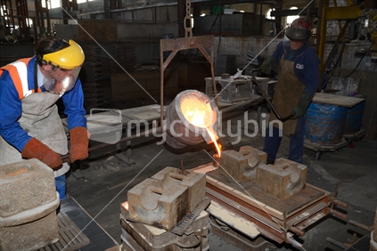 Foundrymen pour molten iron from the induction furnace into a ladle.