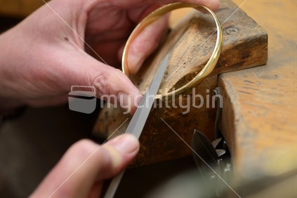A goldsmith files out the join in a bracelet to make it unnoticeable. Filings are collected for recycling.
