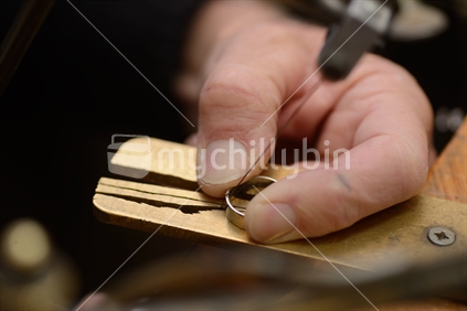 A goldsmith uses a fine saw to cut a gold ring for resizing