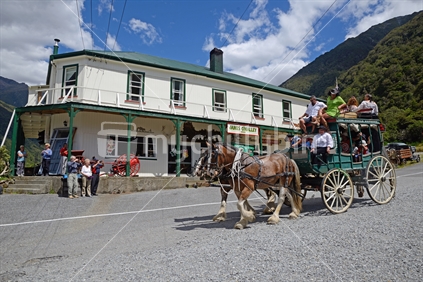 A pair of Clydesdales horses pull a stagecoach of passengers past the Otira hotel, West Coast
