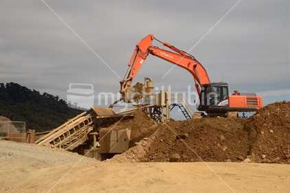 A gold miner feeds paydirt from an open cast mine into the screen that will separate the gold.