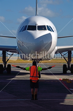 An unidentified ground staff member guides a commercial  jet into place at Auckland Airport