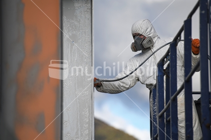 Tradesman spray paints the steel beams on a construction site