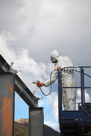 Tradesman spray paints the steel beams on a construction site