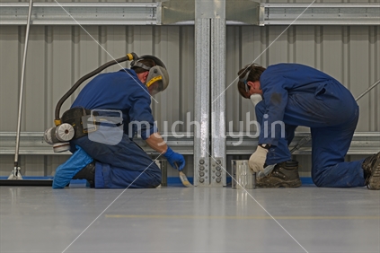 Two tradesmen cut in along the wall with an epoxy flooring compound while the rest of the team uses rollers to finish the job