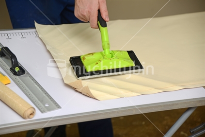 A man spreads glue on the back of wallpaper, ready to decorate a bedroom