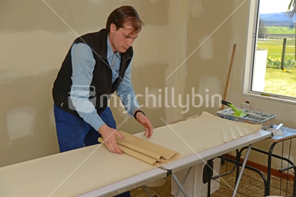 A man rolls up some glued wallpaper, ready to decorate a bedroom