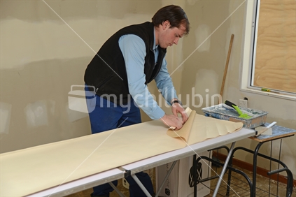 A man folds the ends of wallpaper strips before applying glue