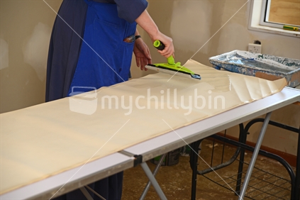 A woman spreads glue on the back of wallpaper, ready to decorate a bedroom