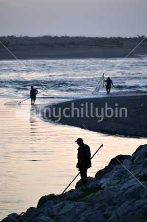HOKITIKA, NEW ZEALAND, OCTOBER 24, 2019: A man uses a scoop net at sunset for catching whitebait at the Hokitika River on the West Coast of the South Island