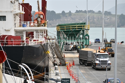 LYTTLETON, NEW ZEALAND, NOVEMBER 21, 2019: Trucks carry away cargo from the Powan (IMO: 9721578, MMSI 477027600)  a Bulk Carrier built in 2016 and currently sailing under the flag of Hong Kong, while docked at Lyttleton harbour..