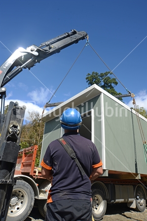GREYMOUTH, NEW ZEALAND, OCTOBER 21, 2020: A crane operator works on lifting a small building from a truck onto its pilings.