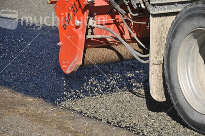 Detail of truck pouring gravel onto fresh asphalt while tar sealing.