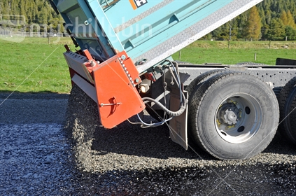 Detail of truck pouring gravel onto fresh asphalt.