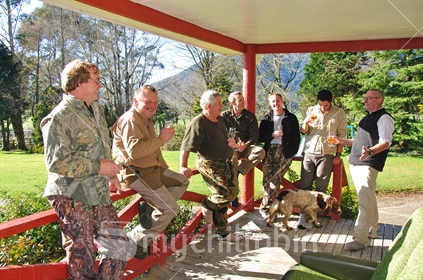 Men relaxing with drinks, and dog,on the verandah before lunch