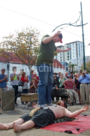 Busker entertaining crowds with a man standing on his chest while laying on broken glass in Christchurch, pre-earthquakes.