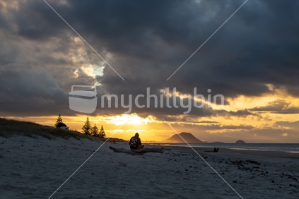 A man siting on a log watching sunset