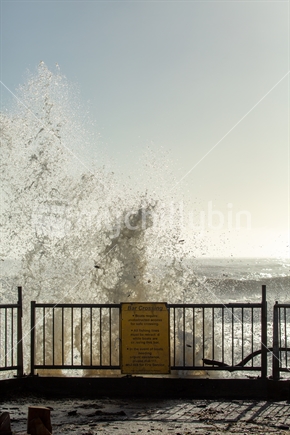 Wave crashing over bar crossing sign (portrait)