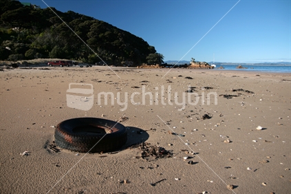 Abandoned tyre, and distant boat trailers parked, on Whatuwhiwhi Beach, Northland, New Zealand. 