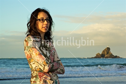Kiwi woman thinking; in front of Ninepin rock, Whatipu, West Coast, Auckland, New Zealand