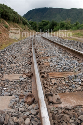 Empty railway tracks, from a low perspective winding off into distant hills.