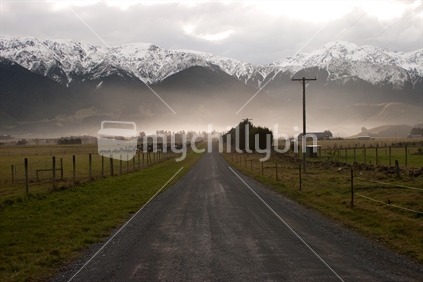 Rural dirt road leads to snowy mountain range