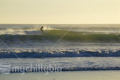 A surfer catches an east-coast wave, early morning at Omaha Beach.