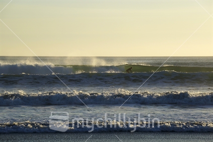A surfer catches an east-coast wave, early morning at Omaha Beach.