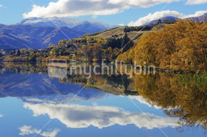 Autumn trees and distant snowy mountains reflected on the surface of Lake Hayes