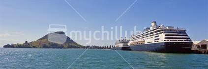 Two cruise ships in Tauranga Harbour with the extinct volcanic cone Mount Maunganui (Mauao), in the background.