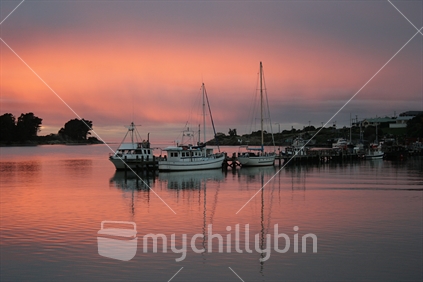 Sunrise over the harbour reflecting fishing boats at Riverton, Southland.