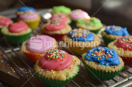 Homemade cupcakes on a tray, with colourful icing and hundred and thousands.