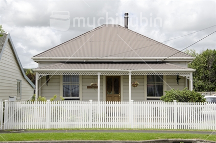 Early weatherboard, double hung window, and corrugated iron home, with a white picket fence.