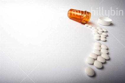 White pills spill out from an amber pill bottle to form the shape of New Zealand on a white background.