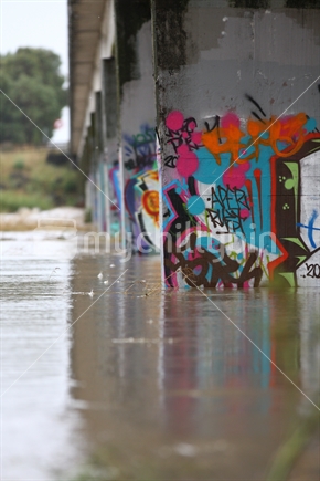 Bridge piles with graffiti, during flood. Ngaruroro River, "Chesterhope Bridge"