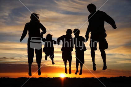 Silhouette family jumping on a New Zealand beach at sunset.