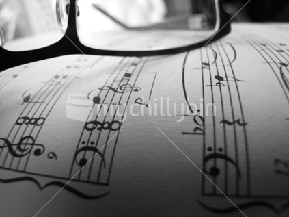 Modern glasses lying on moderately complex classical piano manuscript. Implied sight reading. Image is in black and white.