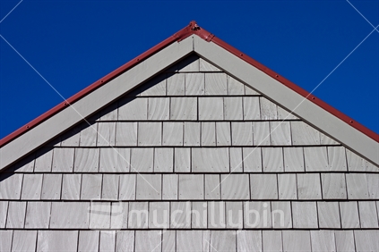 Gable end of house showing shingles under blue sky.