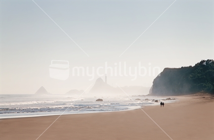 A couple walking along a deserted Oakura beach at sunrise. (focus near surf)
